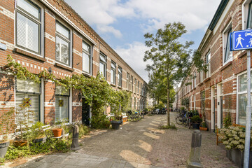 A picturesque urban street showcasing a blend of brick architecture and vibrant greenery, creating a serene atmosphere. The path is lined with potted plants and trees.