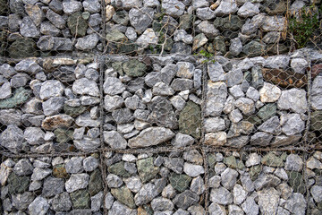 gabion wall, showcasing the texture of the grey stones and the wire mesh. The image highlights the detailed pattern and rugged nature