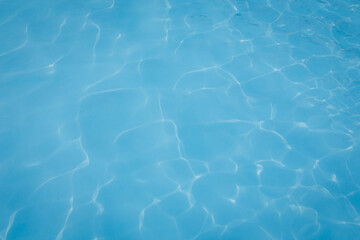 Close-up of clear blue swimming pool water with gentle sunlight reflections creating soft, abstract patterns on the surface, conveying a sense of calm and relaxation.