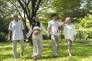 Fototapeta premium Multi-Generational Family Walking Together Outdoors in a Lush Green Garden. A joyful moment of a family strolling through a vibrant park, bonding across generations.