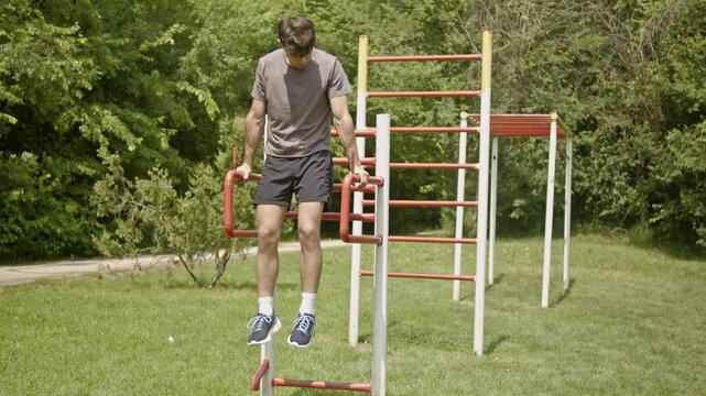 Fit, male, sports person doing dips using parallel bars in a sunny park.