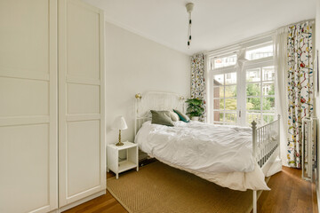 A stylish bedroom featuring a white bed, contemporary furnishings, and large windows letting in natural light, creating a warm ambiance.