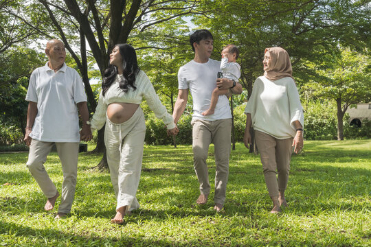 Multi-Generational Family Walking Together Outdoors in a Lush Green Garden. A joyful moment of a family strolling through a vibrant park, bonding across generations. - Powered by Adobe