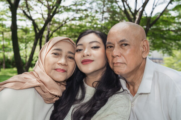 cheerful family takes a selfie together in a beautiful green park, radiating joy and togetherness during a sunny day. The serene background emphasizes the peace and happiness of this cherished moment.