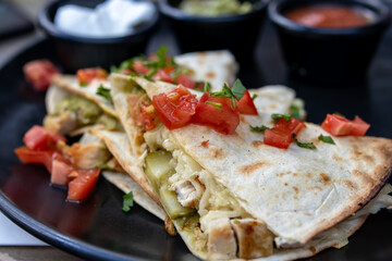 Delicious Chicken Quesadilla with Toppings on a Black Plate