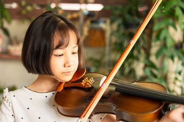 Asian girl passionately plays the violin, demonstrating focus and dedication during a music lesson. Her precise movements and deep concentration highlight her growing talent as a young musician.