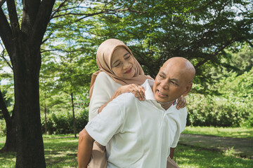 Fototapeta premium Elderly couple shares a joyful moment outdoors in a serene park setting featuring lush greenery and clear skies, symbolizing love, happiness, and togetherness.