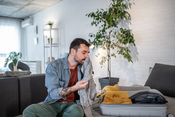 Man smelling clothes while packing suitcase at home