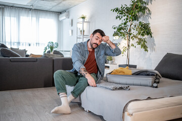 Stressed man packing clothes into a suitcase at home