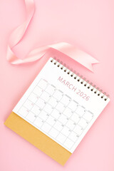 March 2026 desk calendar with pink ribbon, Flat lay.
