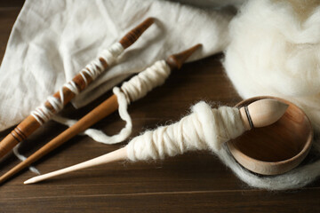 Spindles and soft white wool on wooden table, closeup