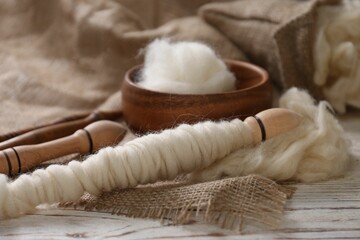 Soft white wool and spindles on wooden table, closeup