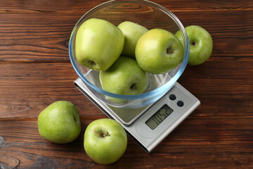 Electronic kitchen scale with bowl of green apples on wooden table