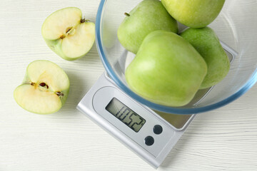 Electronic kitchen scale with bowl of green apples on white wooden table, flat lay