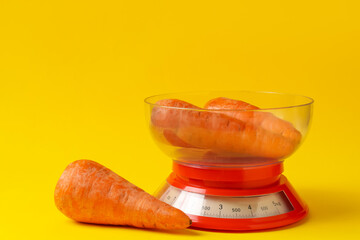 Kitchen scale with fresh carrots on yellow background, closeup