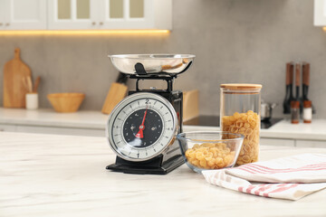 Retro mechanical kitchen scale and raw pasta on white marble table indoors
