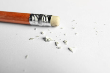 Pencil with eraser and scraps on white sheet of paper, closeup