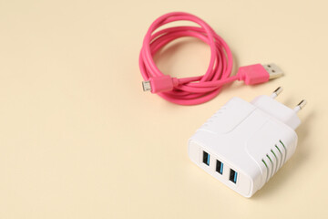 USB power adapter and charge cable on beige background, closeup. Space for text