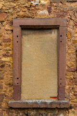 Old stone wall with a blank window frame in a rustic building showing signs of wear in sunny weather