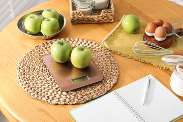 Electronic kitchen scale, products and stationery on wooden table indoors