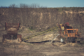 Old mining equipment abandoned in a barren landscape surrounded by sparse vegetation during...