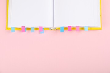 Book with colorful tabs on pink background, top view. Space for text