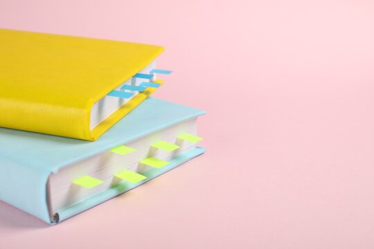 Books with colorful tabs on pink background, closeup. Space for text
