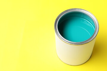Can of turquoise paint on yellow background, closeup. Space for text