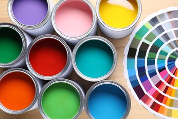 Cans of bright paints and color palettes on wooden table, flat lay