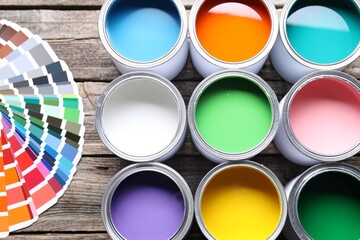 Cans of bright paints and color palettes on wooden table, flat lay