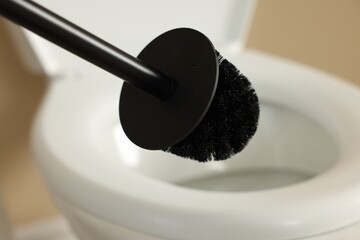 Cleaning toilet bowl with black brush indoors, closeup