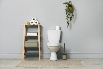 Ceramic toilet bowl, brush and paper near grey wall indoors