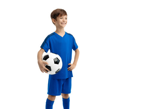 Confident young boy in blue sport outfit posing with classic soccer ball over white background