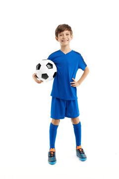 Confident young boy in blue sport outfit posing with classic soccer ball over white background