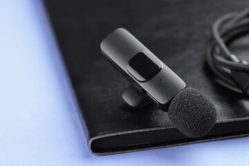 Lavalier microphone, cord and notebook on light blue background, closeup