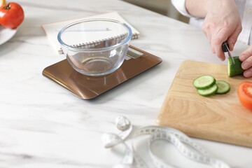 Woman weighting ingredients while cooking salad at white table indoors, closeup