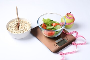Electronic kitchen scales with salad, apple, oats and measuring tape isolated on white