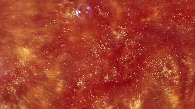 liquid with dissolved particles of orange candurin is bubbling and mixing vigorously. abstract bright background