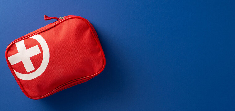 Red-colored banner first aid kit displayed with a plain blue background, symbolizing emergency readiness and medical supplies
