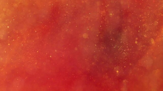 liquid with dissolved particles of red orange candurin and bubbles slowly moves and shines. abstract bright background