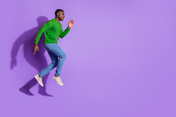 Side view of a young man in casual clothing jumping with energy against a purple background