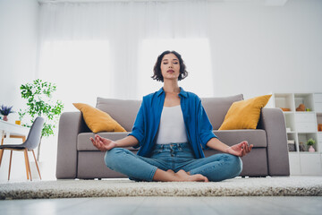 Young woman meditating in a bright living room, sitting cross legged on the floor in a serene home environment