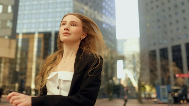 Young attractive long haired woman is hurrying to a meeting or to work, looking at the clock in her smartphone and running along the city street in the business center of Paris