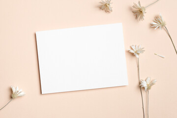 Horizontal white blank card on a beige background surrounded by delicate dried white flowers, ideal for wedding invitations, menus, or romantic stationery designs.