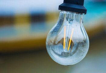 Closeup of a hanging outdoors incandescent glass lamp with glowing filaments.  Vintage style light bulb. Copy space. Blurred background. energy, innovation, electricity, sustainability, illumination