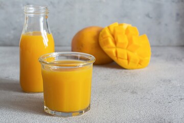 Fresh mango juice in a glass with mango slice on a gray background. Exotic drink, Trending colors.