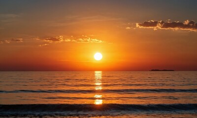Beautiful sunset over calm ocean with reflections and soft clouds on a warm evening sky