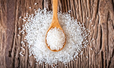 Rice grains scattered on wooden surface with a wooden spoon holding a small portion