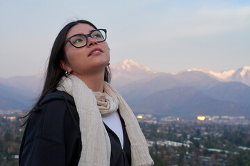 Young woman in glasses looking up thoughtfully against a snowy mountain backdrop