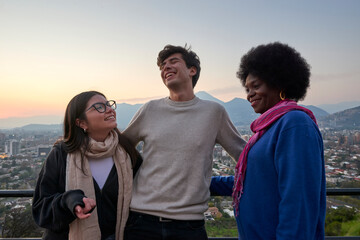 A group of friends smile and embrace while enjoying the sunset over a city, creating a joyful and warm scene